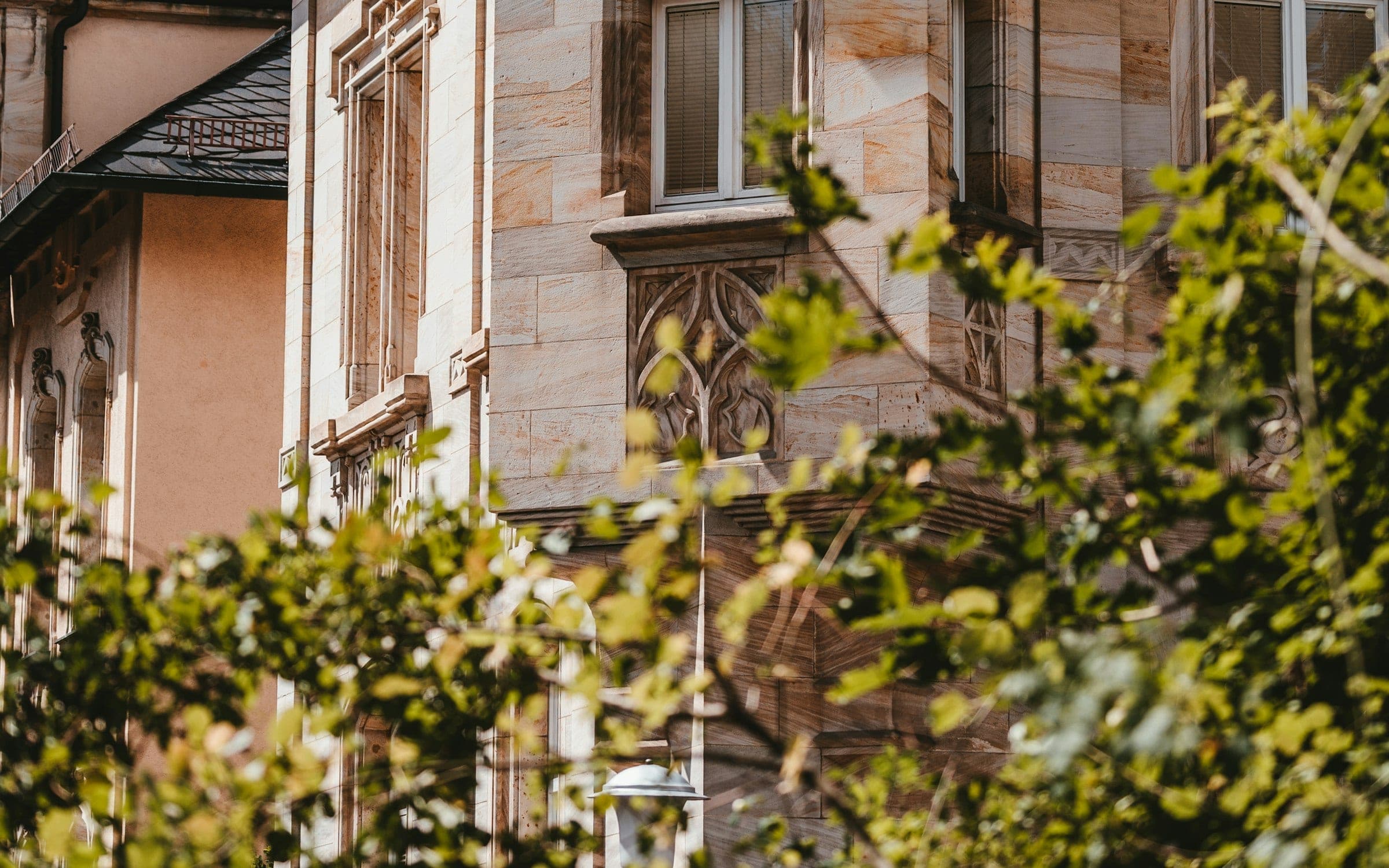 Renovierte Sandstein-Altbaufassade mit Ornamenten hinter sommerlichem Grün